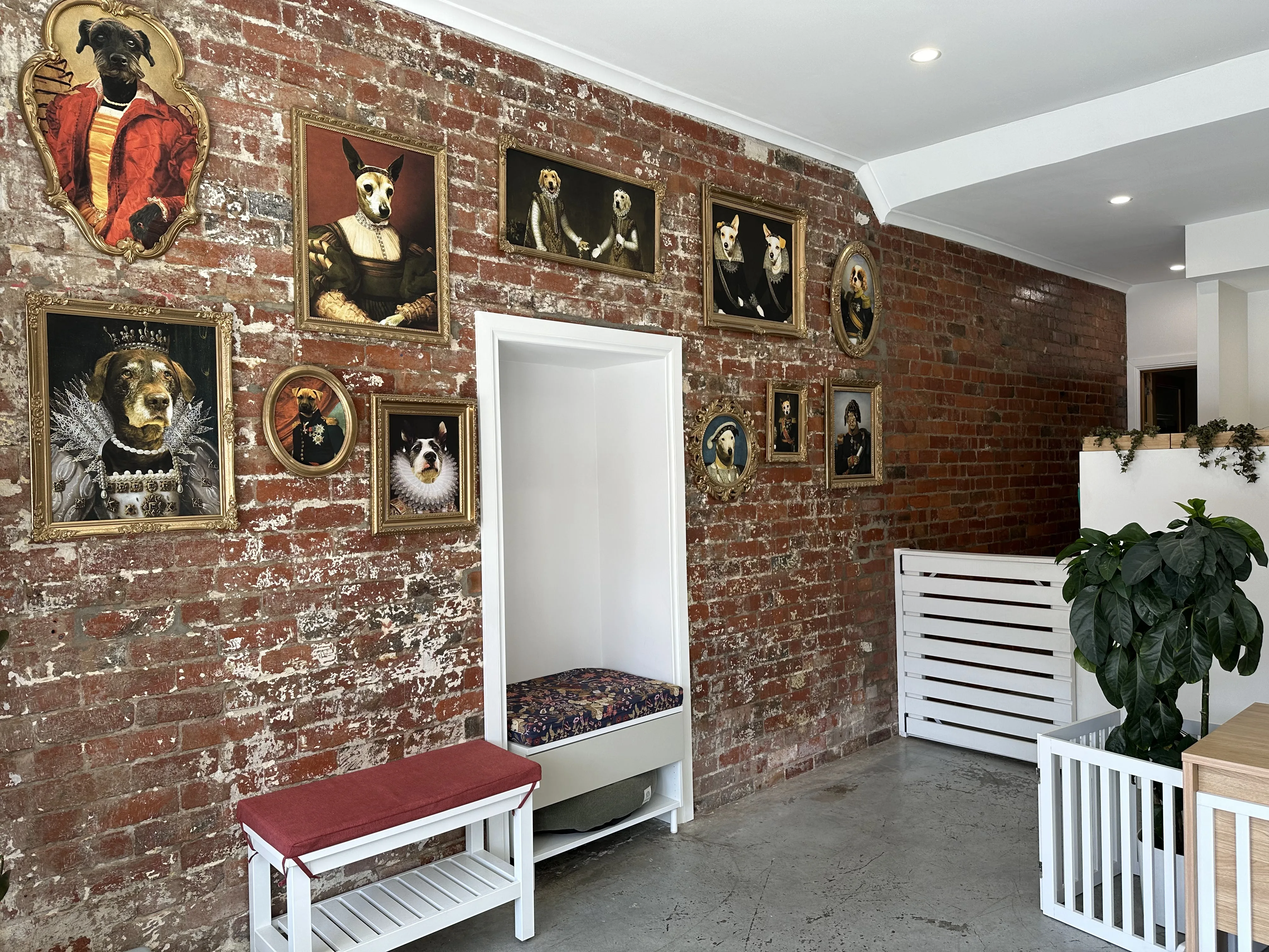 Salon waiting area with wall of gilded renaissance dog portraits on exposed brick, red-velvet bench